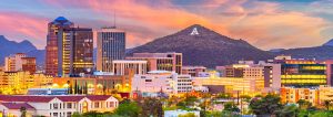 Sunset view of a city skyline with a large 'A' on a nearby mountain.