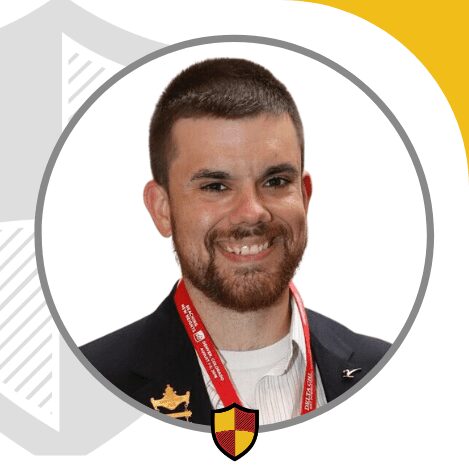 Smiling man in a suit with a shield emblem on his lapel.