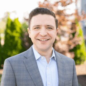 Smiling man in suit outdoors with trees.