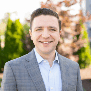 Smiling man in suit outdoors with trees.