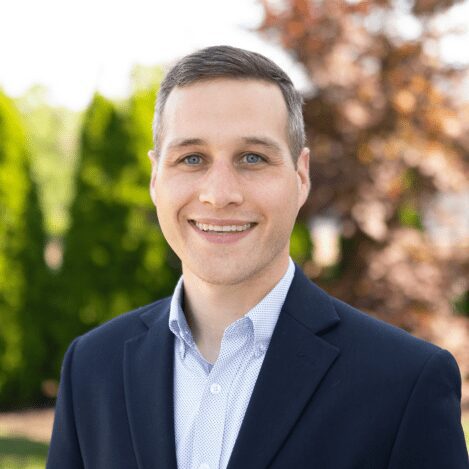 Smiling person in a suit outdoors.