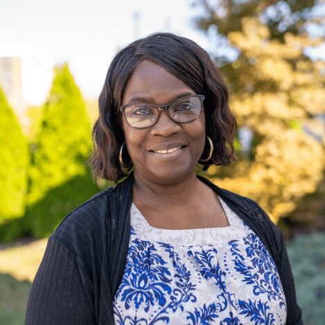 Woman smiling outdoors with glasses and trees.