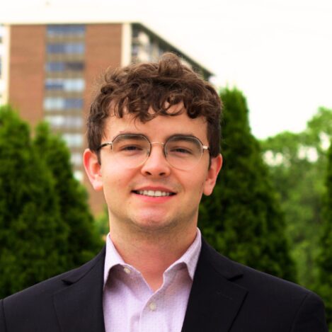 Young man smiling in a suit outdoors.