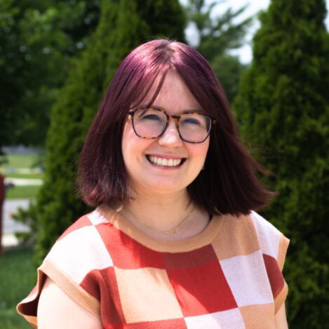 Smiling woman with glasses in outdoor setting.