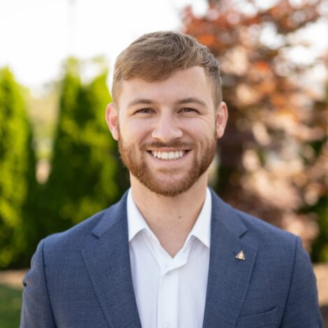 Smiling man in a blue blazer outdoors.